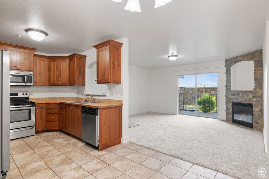 Kitchen featuring stainless steel appliances, a stone fireplace, sink, light colored carpet, and a textured ceiling