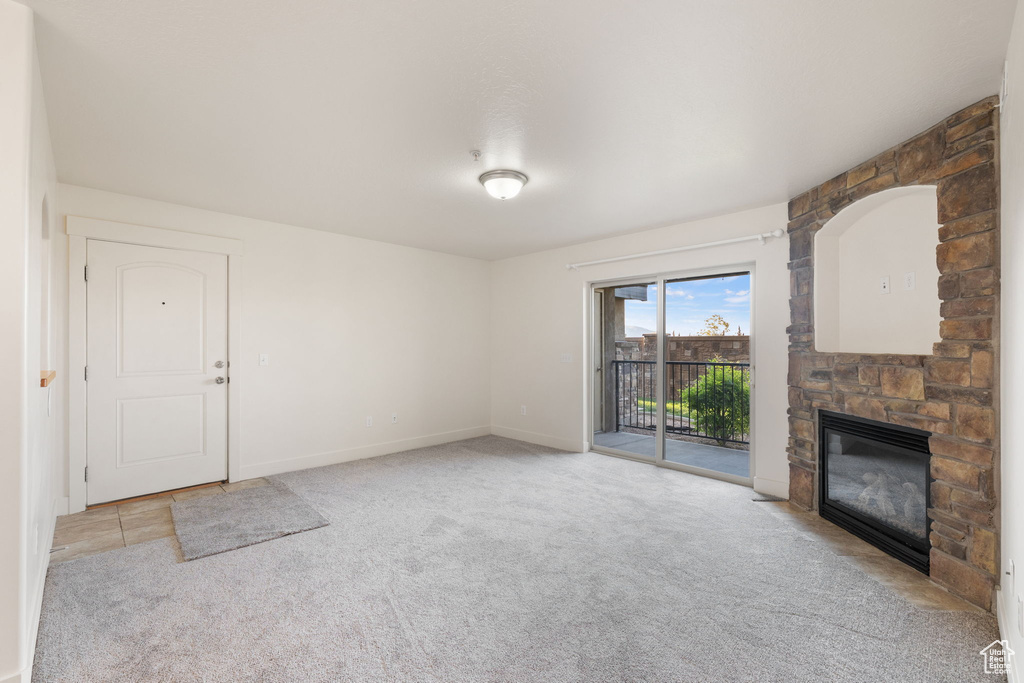 Unfurnished living room featuring a stone fireplace and light colored carpet