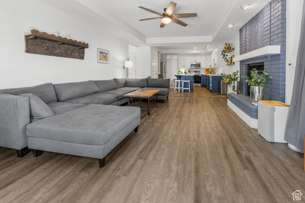 Living room with ceiling fan, a fireplace, wood-type flooring, and a tray ceiling