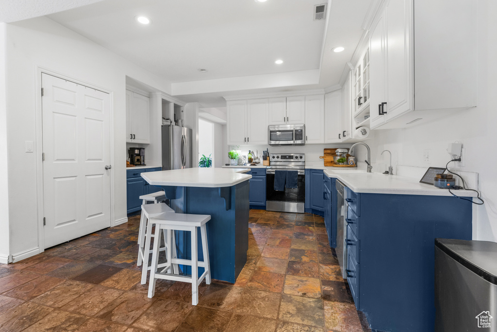 Kitchen featuring a breakfast bar, white cabinetry, blue cabinetry, and stainless steel appliances