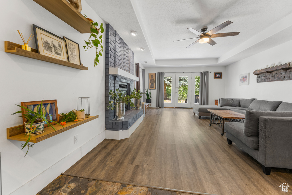 Living room featuring french doors, dark hardwood / wood-style floors, a brick fireplace, ceiling fan, and a raised ceiling