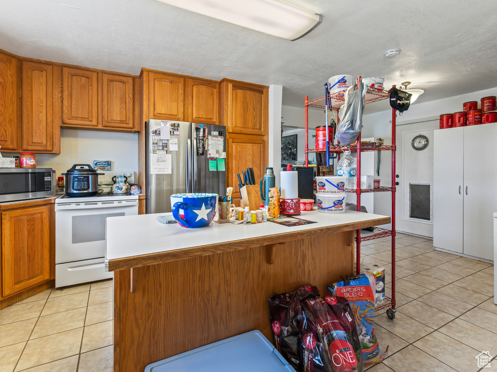 Kitchen with light tile patterned flooring, a center island, appliances with stainless steel finishes, and a kitchen breakfast bar