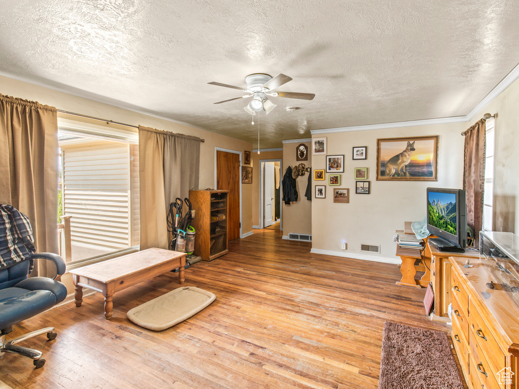 Living room featuring a textured ceiling, ornamental molding, hardwood / wood-style floors, and ceiling fan