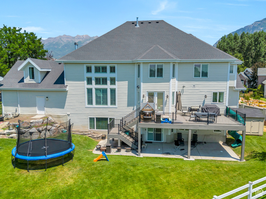 Back of house featuring a patio, a deck with mountain view, a trampoline, and a yard