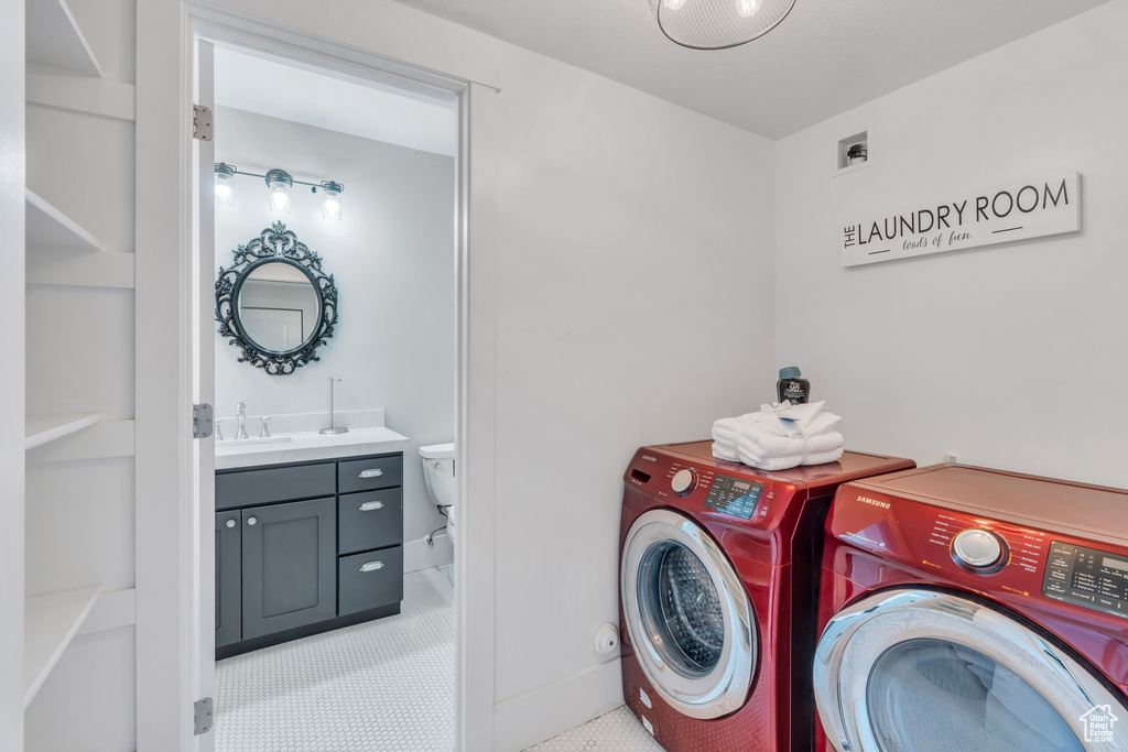 Clothes washing area with light tile patterned flooring, washer and dryer, and sink