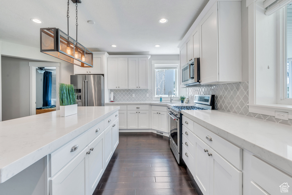 Kitchen featuring hanging light fixtures, premium appliances, white cabinets, and backsplash