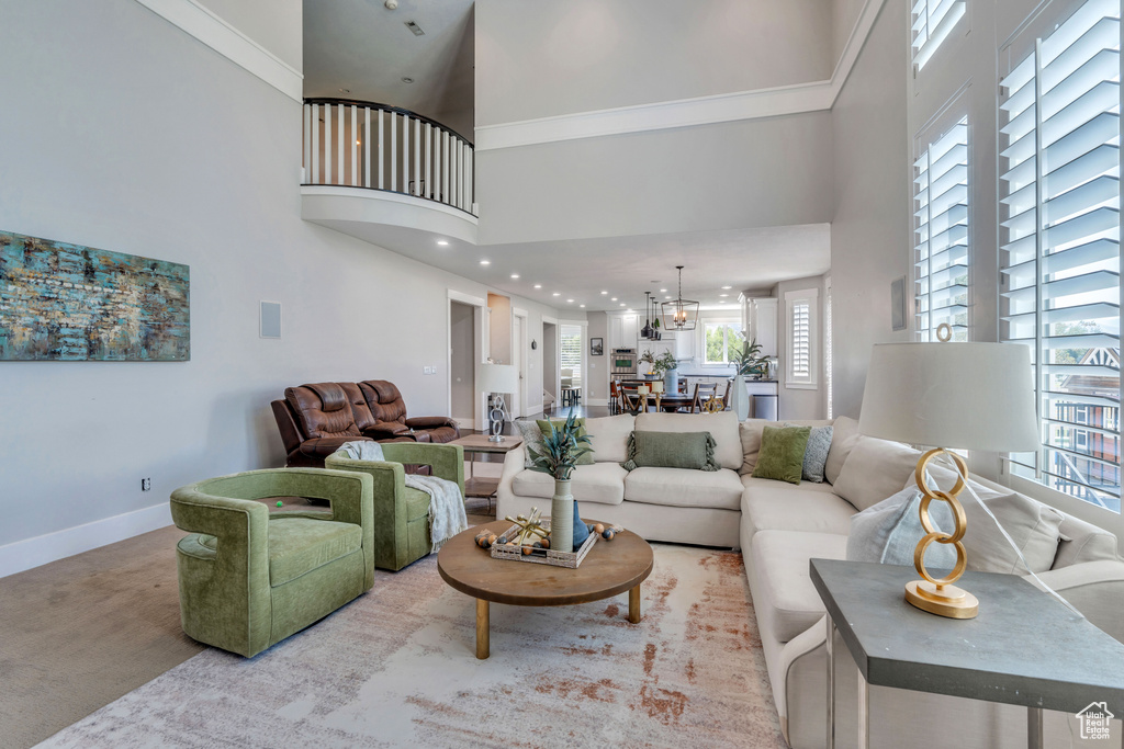 Living room featuring carpet floors, a high ceiling, crown molding, and a notable chandelier