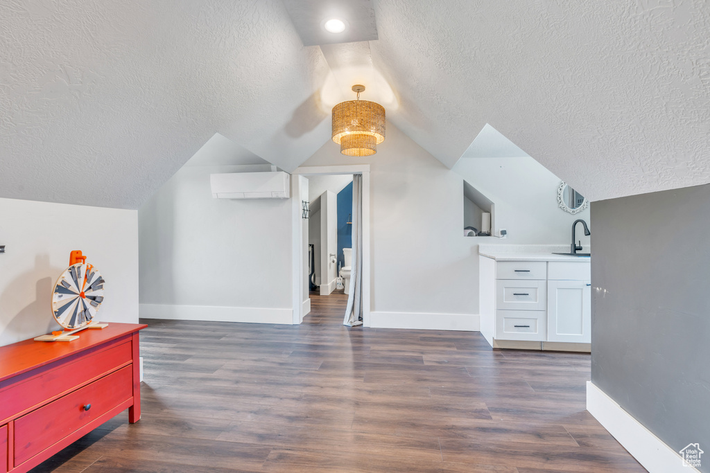 Additional living space featuring sink, a textured ceiling, lofted ceiling, a wall mounted air conditioner, and dark hardwood / wood-style flooring