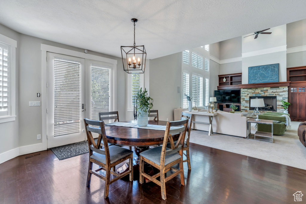 Carpeted dining space with a fireplace, ceiling fan with notable chandelier, a wealth of natural light, and a textured ceiling