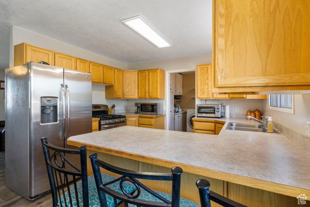 Kitchen with appliances with stainless steel finishes, washing machine and clothes dryer, sink, kitchen peninsula, and wood-type flooring