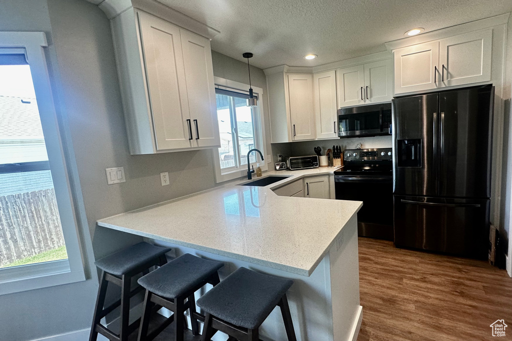 Kitchen featuring black appliances, hardwood / wood-style flooring, white cabinets, plenty of natural light, and sink