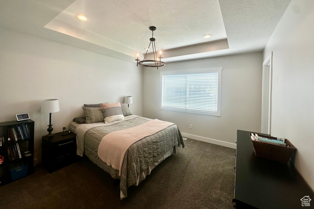 Bedroom with an inviting chandelier, a textured ceiling, dark carpet, and a tray ceiling