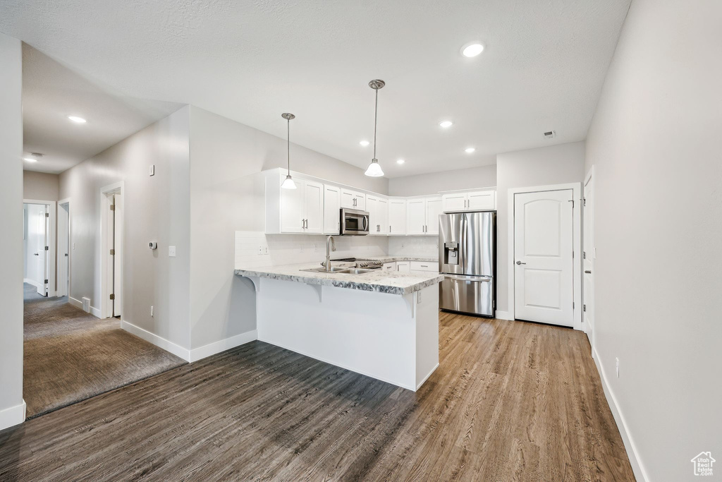 Kitchen with stainless steel appliances, white cabinets, kitchen peninsula, hanging light fixtures, and wood-type flooring