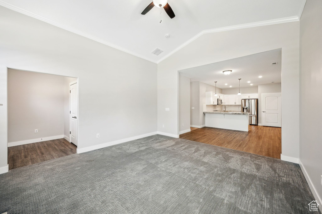 Unfurnished living room with ornamental molding, wood-type flooring, ceiling fan, and vaulted ceiling