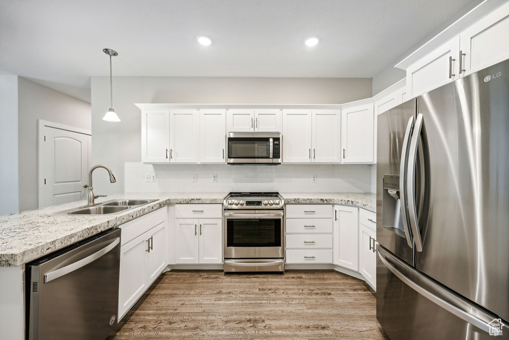 Kitchen with kitchen peninsula, stainless steel appliances, light hardwood / wood-style floors, pendant lighting, and sink