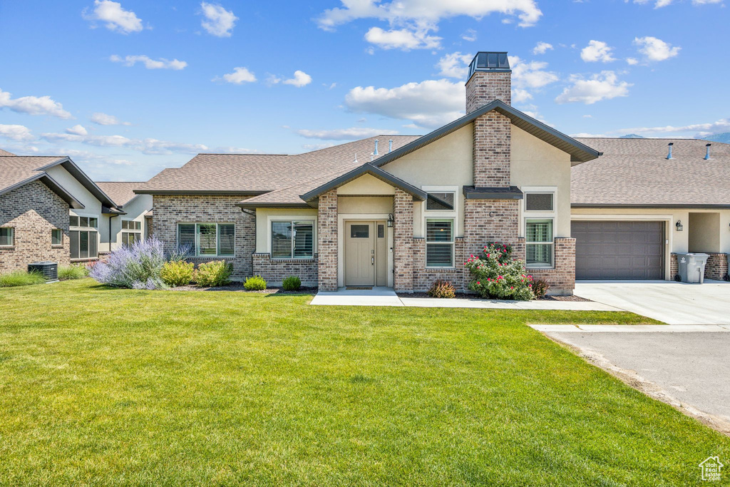 View of front of house featuring a garage, central air condition unit, and a front lawn