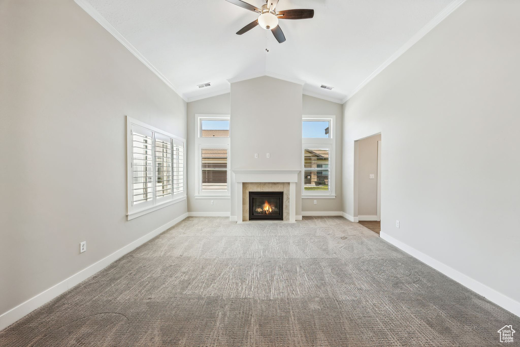 Unfurnished living room featuring vaulted ceiling, a tile fireplace, crown molding, carpet flooring, and ceiling fan