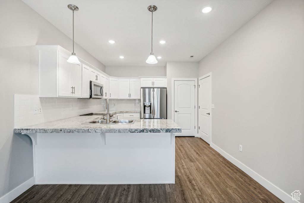 Kitchen with appliances with stainless steel finishes, kitchen peninsula, decorative light fixtures, decorative backsplash, and dark hardwood / wood-style floors