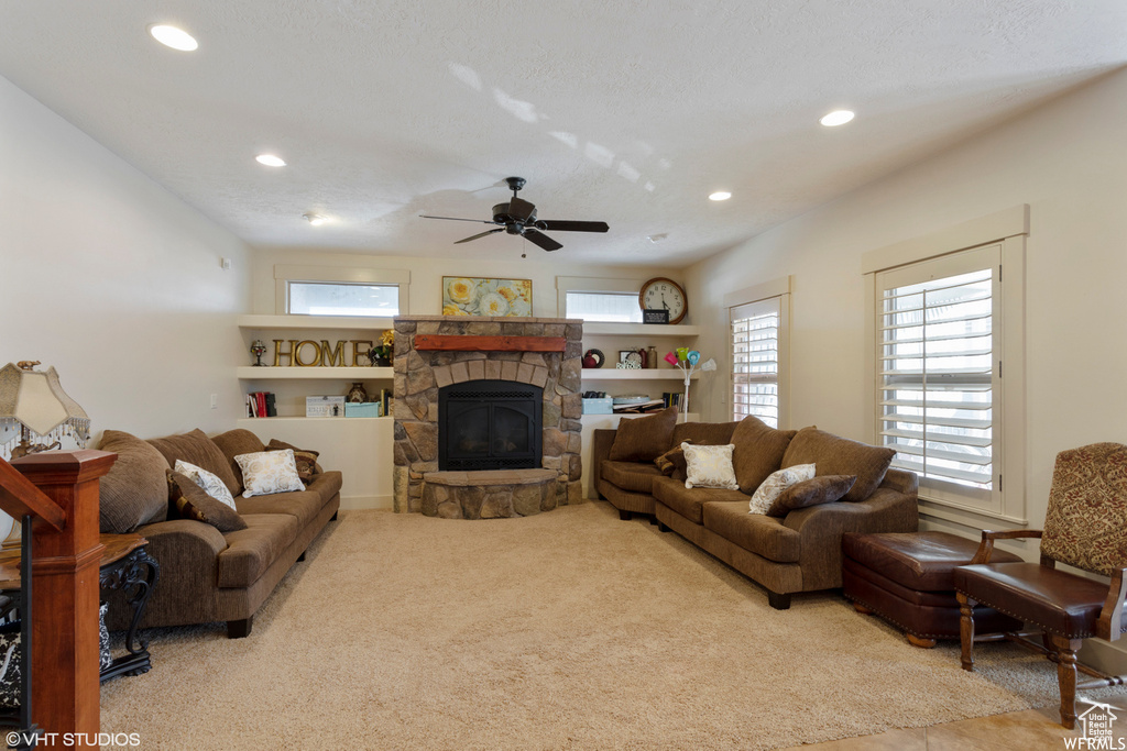 Living room with a stone fireplace, light carpet, and ceiling fan