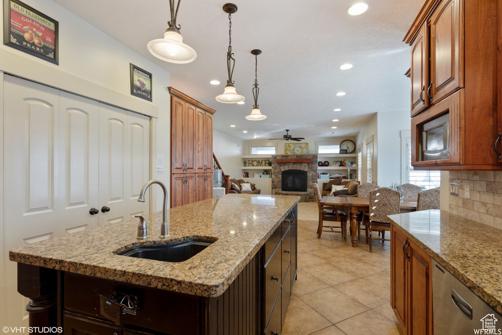 Kitchen with a stone fireplace, sink, backsplash, a kitchen island with sink, and ceiling fan