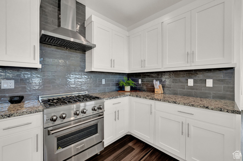 Kitchen with tasteful backsplash, dark hardwood / wood-style flooring, white cabinets, wall chimney exhaust hood, and stainless steel range