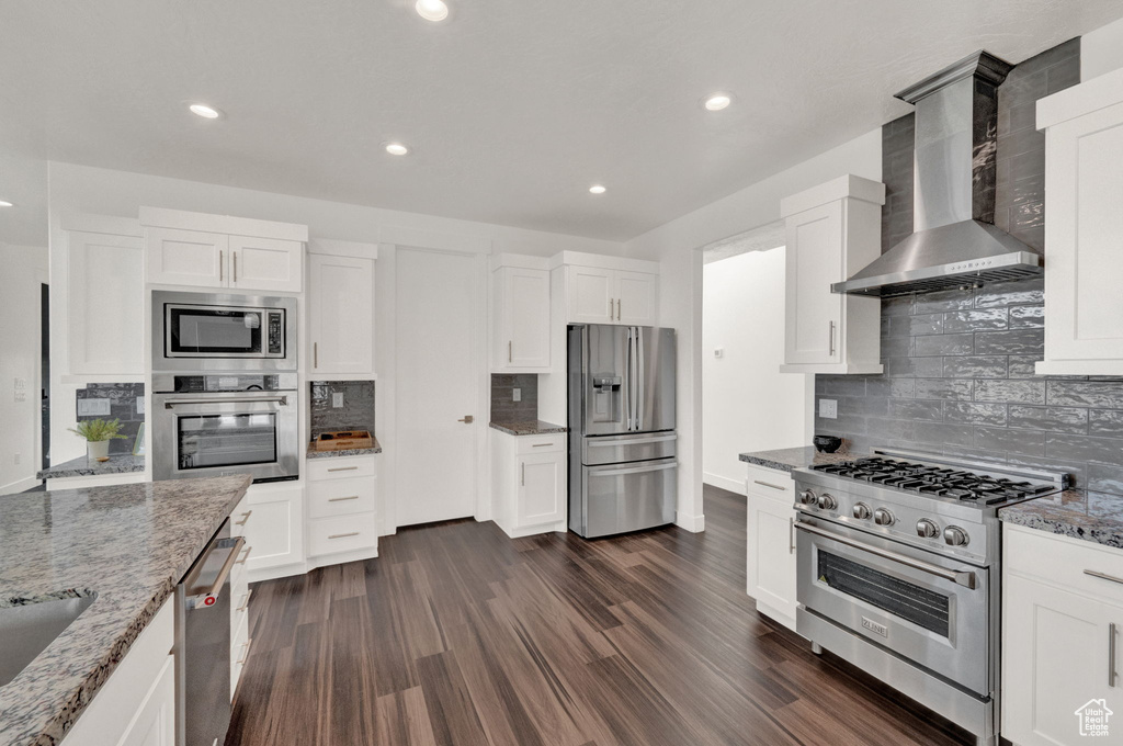 Kitchen with stainless steel appliances, wall chimney range hood, decorative backsplash, dark hardwood / wood-style floors, and light stone countertops