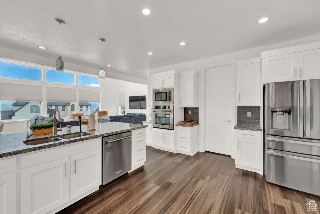 Kitchen with dark hardwood / wood-style floors, appliances with stainless steel finishes, dark stone countertops, and sink