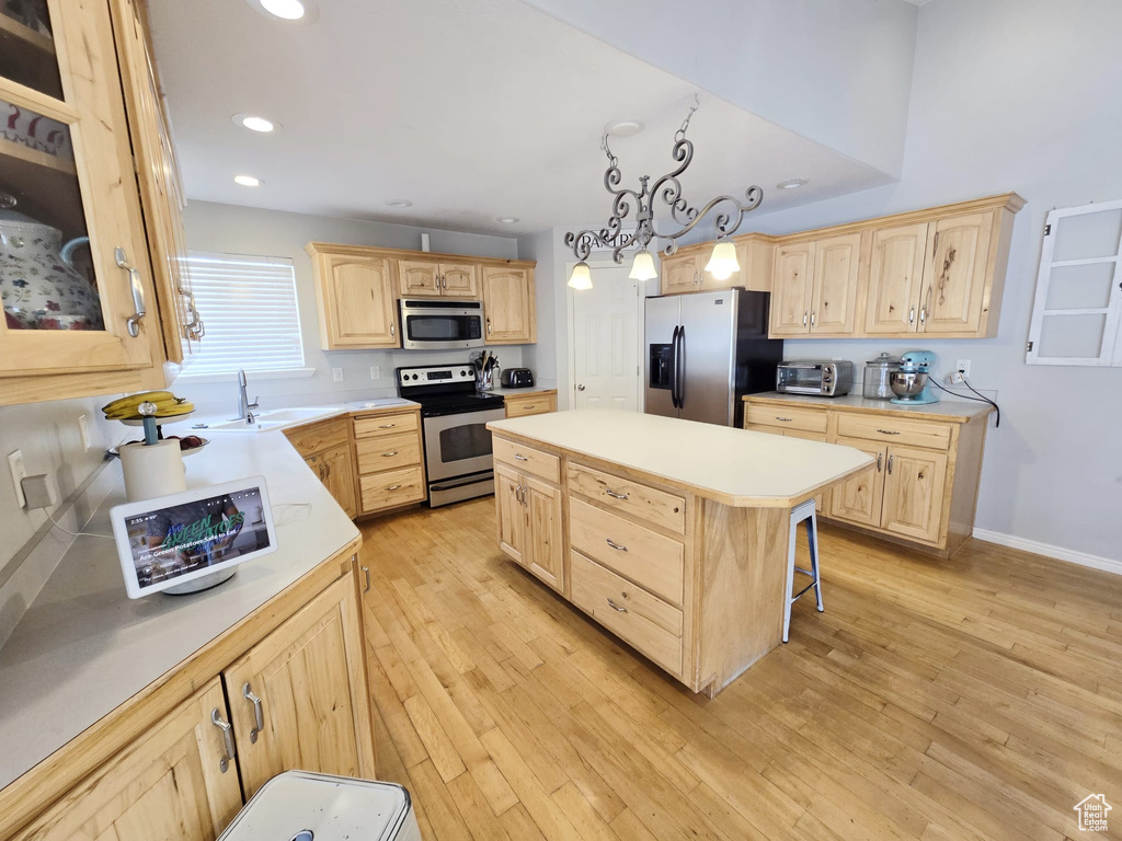 Kitchen featuring light wood-type flooring, light brown cabinets, a breakfast bar area, a kitchen island, and appliances with stainless steel finishes