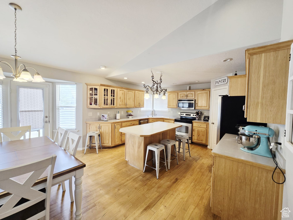 Kitchen with stainless steel appliances, light brown cabinets, light wood-type flooring, lofted ceiling, and a center island