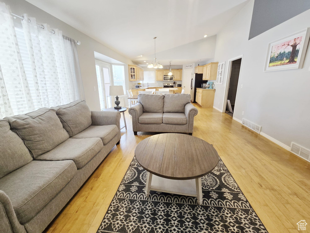 Living room featuring high vaulted ceiling, light wood-type flooring, and a chandelier