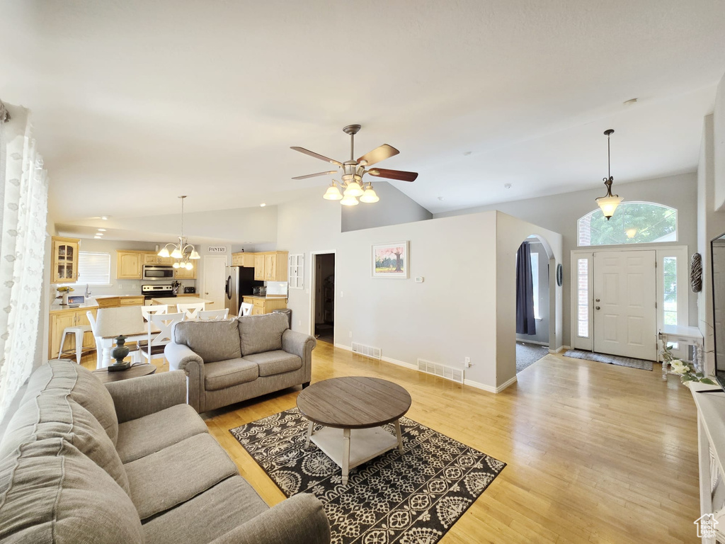 Living room with high vaulted ceiling, light wood-type flooring, and ceiling fan with notable chandelier