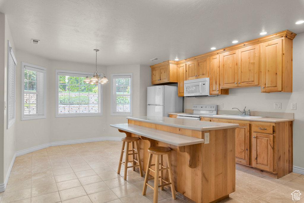 Kitchen featuring white appliances, a chandelier, light tile patterned floors, a center island, and hanging light fixtures