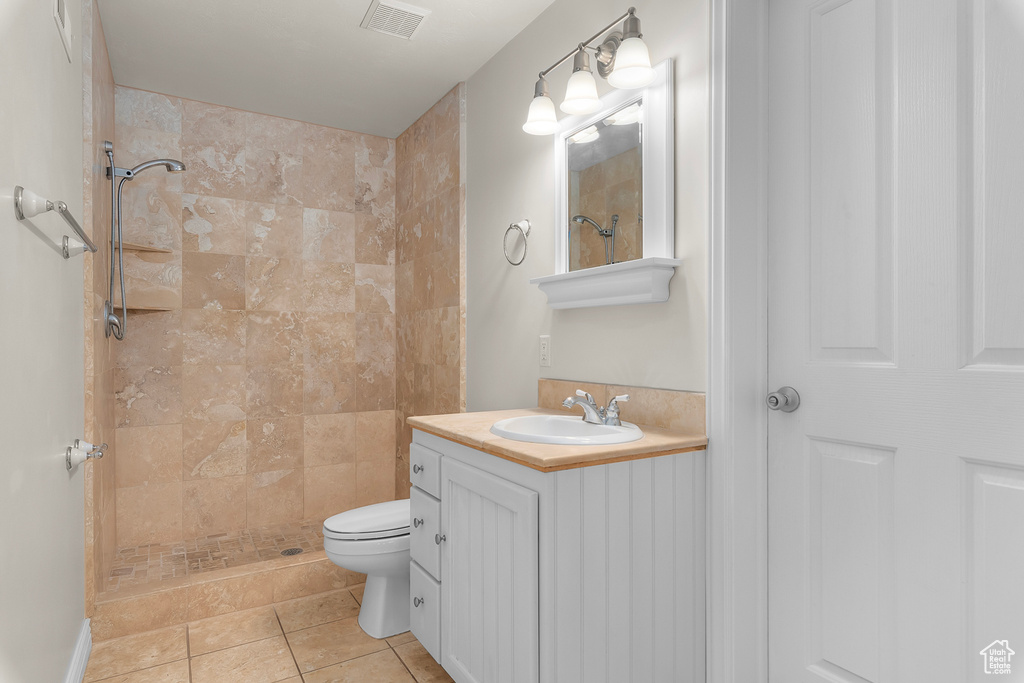 Bathroom featuring vanity, a tile shower, tile patterned flooring, and toilet