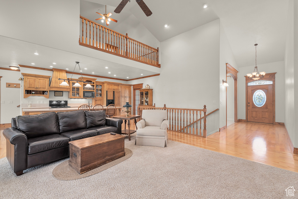 Living room with high vaulted ceiling, ceiling fan with notable chandelier, light hardwood / wood-style flooring, and ornamental molding