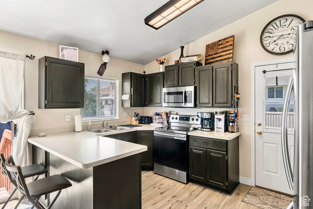 Kitchen featuring light wood-type flooring, kitchen peninsula, appliances with stainless steel finishes, vaulted ceiling, and sink