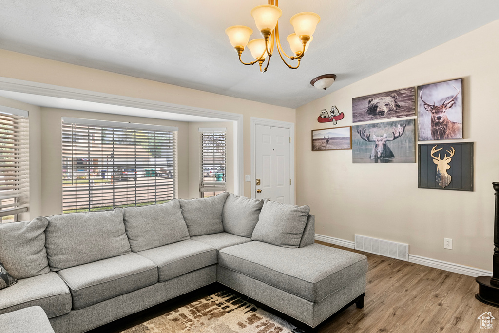 Living room featuring hardwood / wood-style flooring, a notable chandelier, and vaulted ceiling