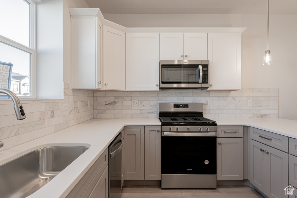 Kitchen featuring backsplash, appliances with stainless steel finishes, white cabinetry, gray cabinets, and sink