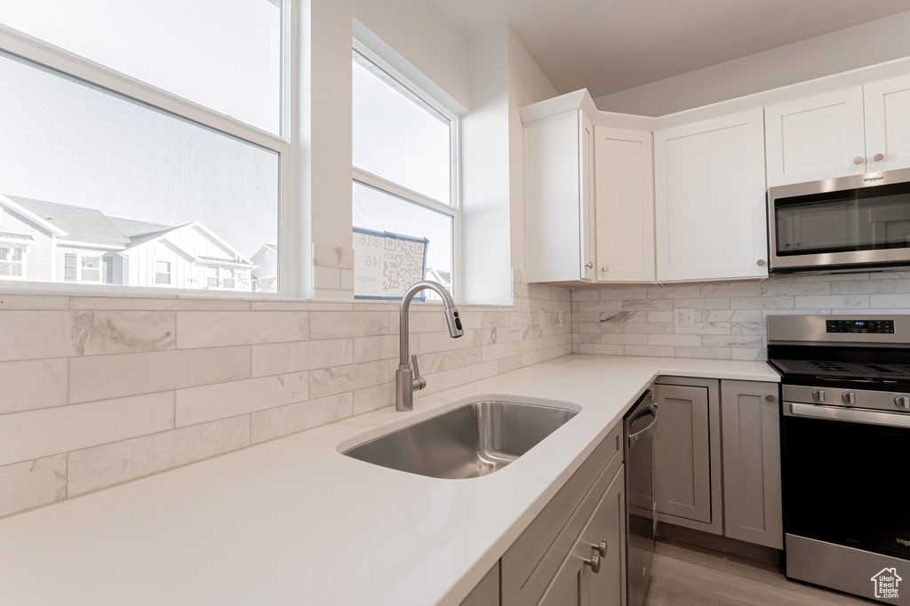 Kitchen with gray cabinetry, sink, backsplash, stainless steel appliances, and white cabinets