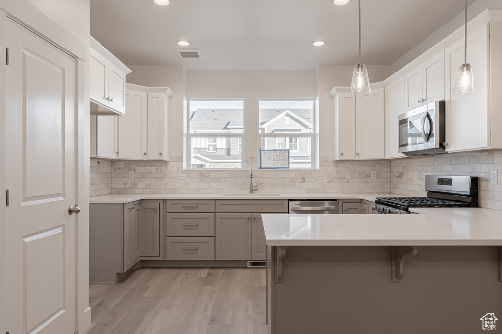 Kitchen with white cabinets, light hardwood / wood-style flooring, sink, pendant lighting, and stainless steel appliances