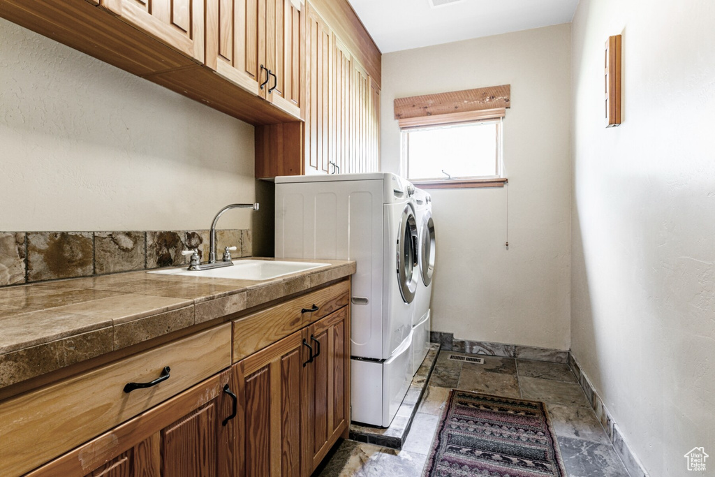 Clothes washing area featuring sink, cabinets, tile patterned flooring, and washing machine and clothes dryer