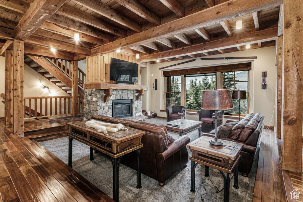 Living room featuring a stone fireplace, wood-type flooring, lofted ceiling with beams, and wooden ceiling