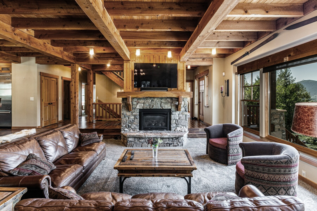 Carpeted living room featuring a stone fireplace, wooden ceiling, and beam ceiling