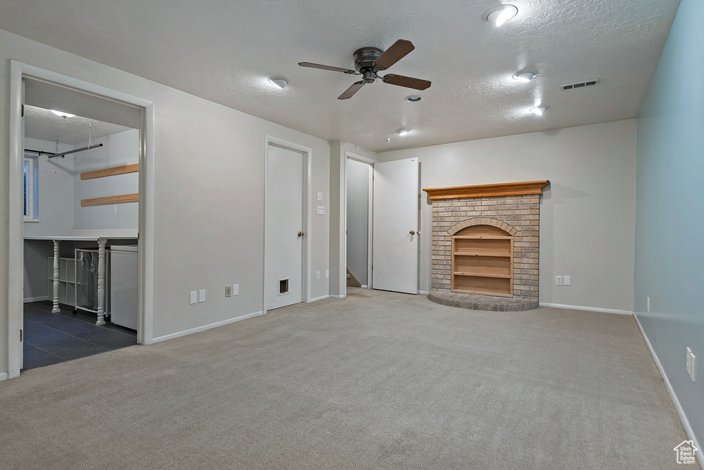 Unfurnished living room with carpet, built in shelves, a brick fireplace, a textured ceiling, and ceiling fan