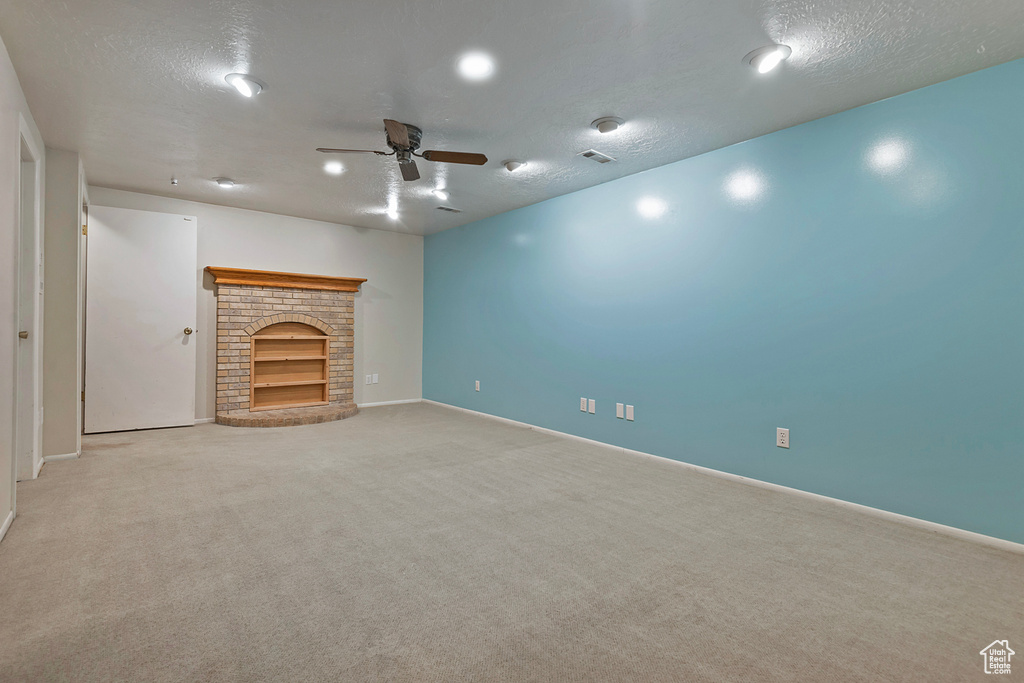 Unfurnished living room with a textured ceiling, built in shelves, carpet floors, ceiling fan, and a brick fireplace