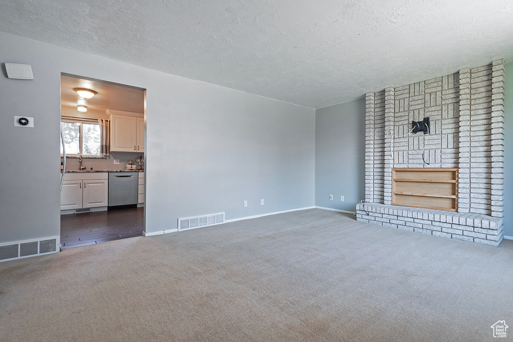 Unfurnished living room with dark carpet, brick wall, sink, and a textured ceiling