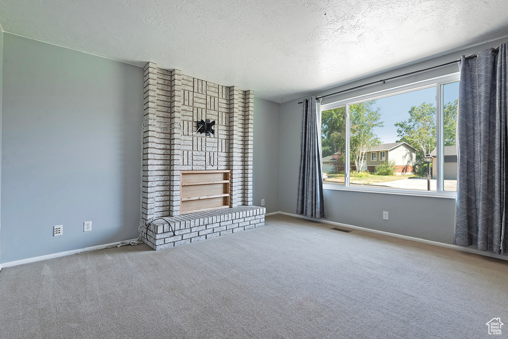 Unfurnished living room featuring carpet, brick wall, and a textured ceiling