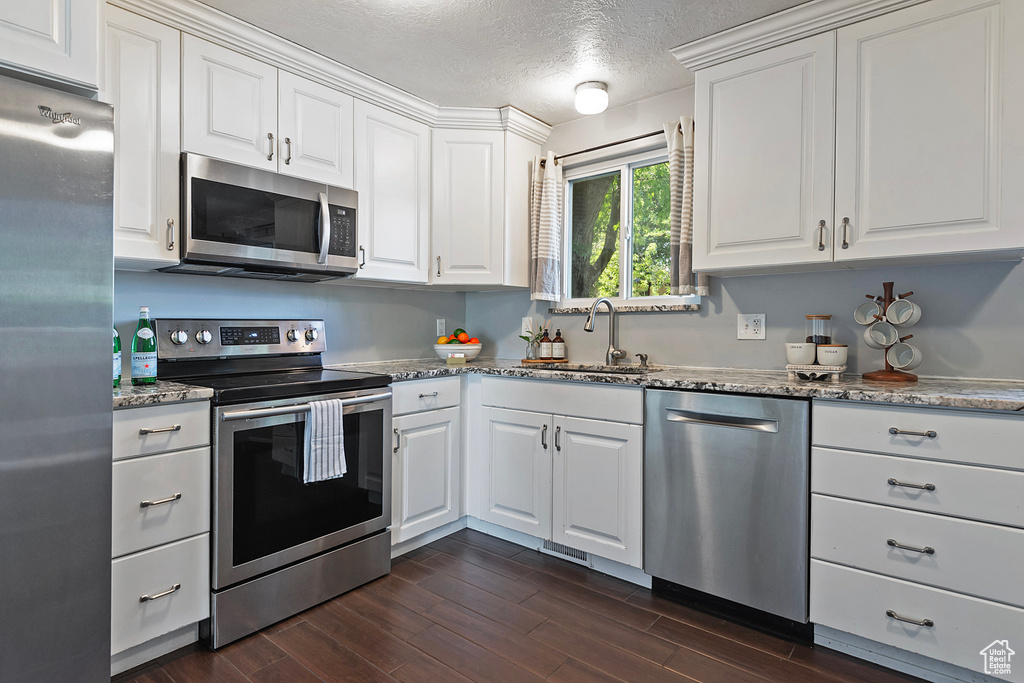 Kitchen with stainless steel appliances, white cabinets, sink, a textured ceiling, and dark hardwood / wood-style flooring