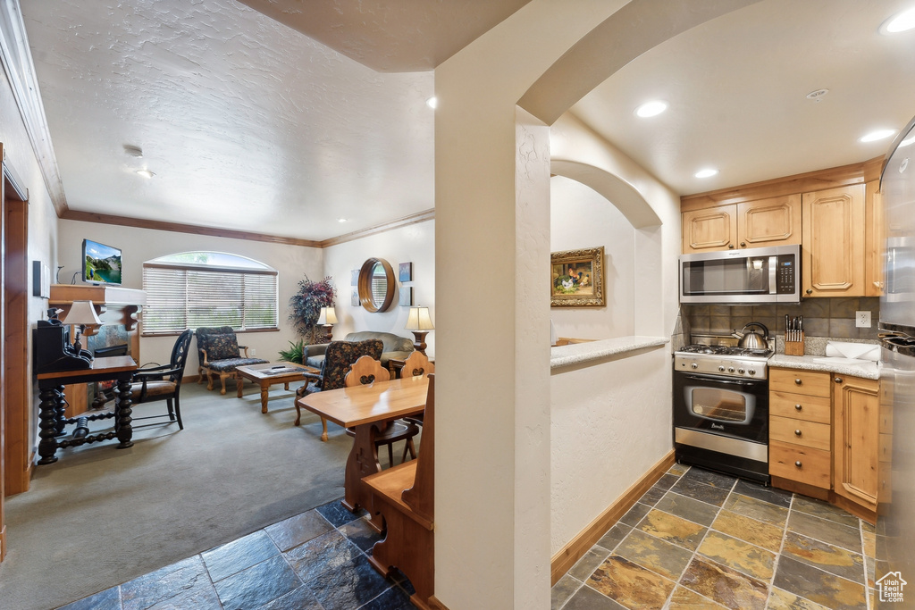 Kitchen with range with gas stovetop, tasteful backsplash, dark tile patterned floors, crown molding, and light brown cabinets