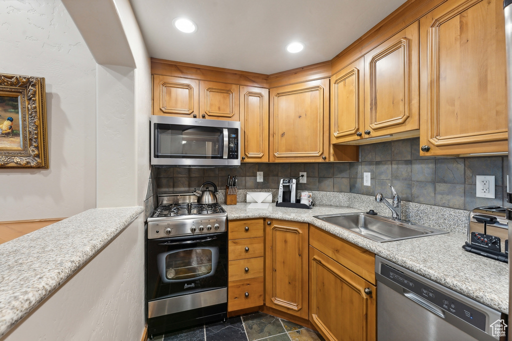 Kitchen with sink, appliances with stainless steel finishes, tasteful backsplash, and dark tile patterned flooring