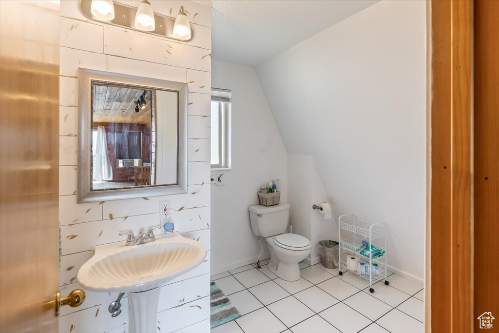 Bathroom featuring lofted ceiling, tile patterned floors, toilet, and sink